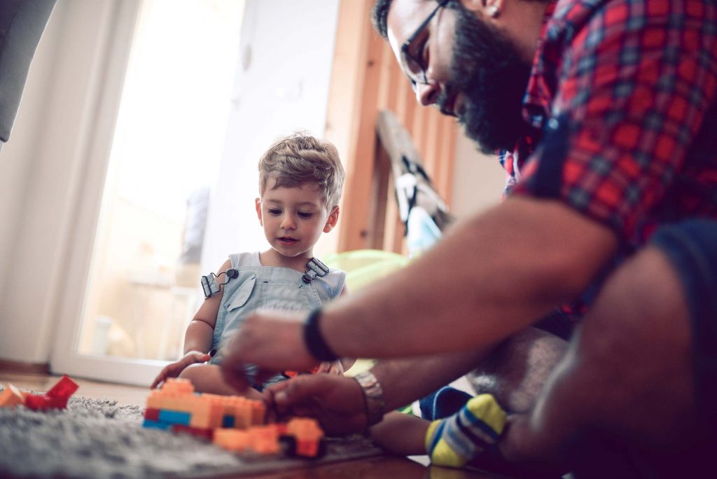 An adult putting together interlocking blocks sitting next to a child who is watching the adult