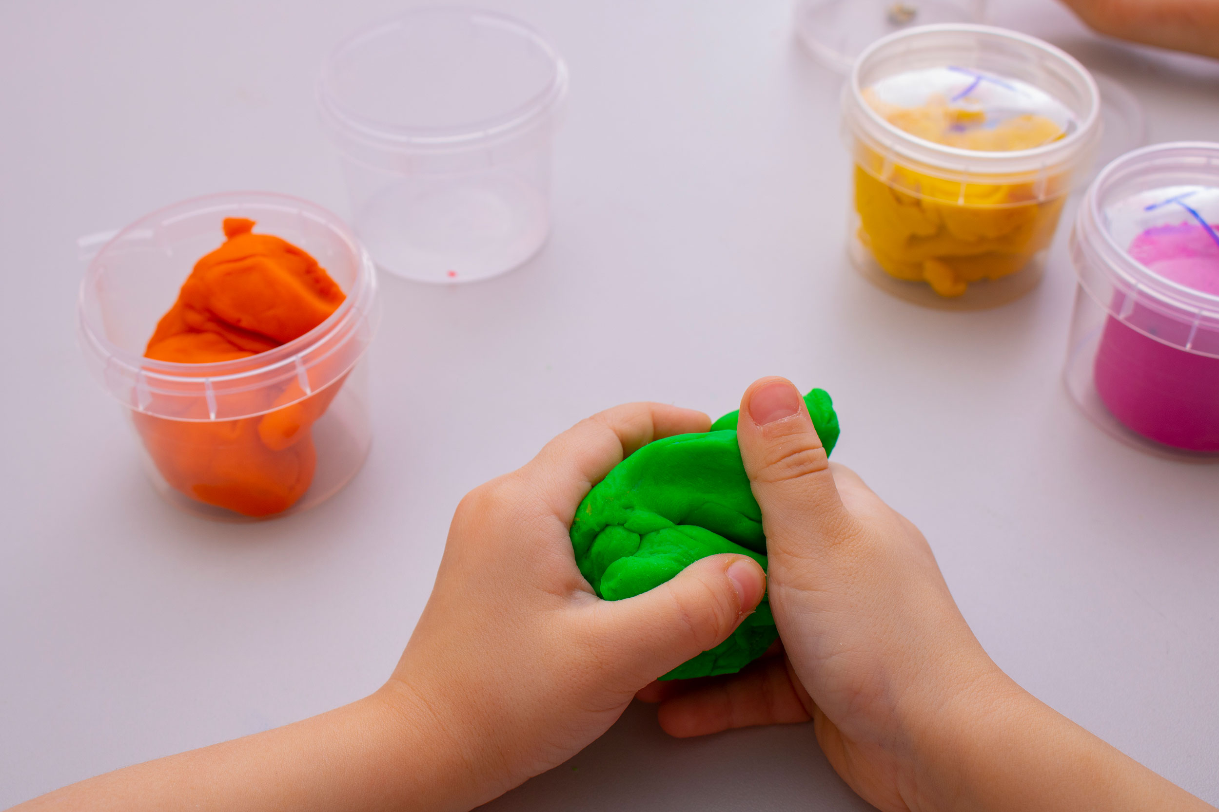 A close up of play dough in cups while a child's hands manipulate a clump of green play dough.

