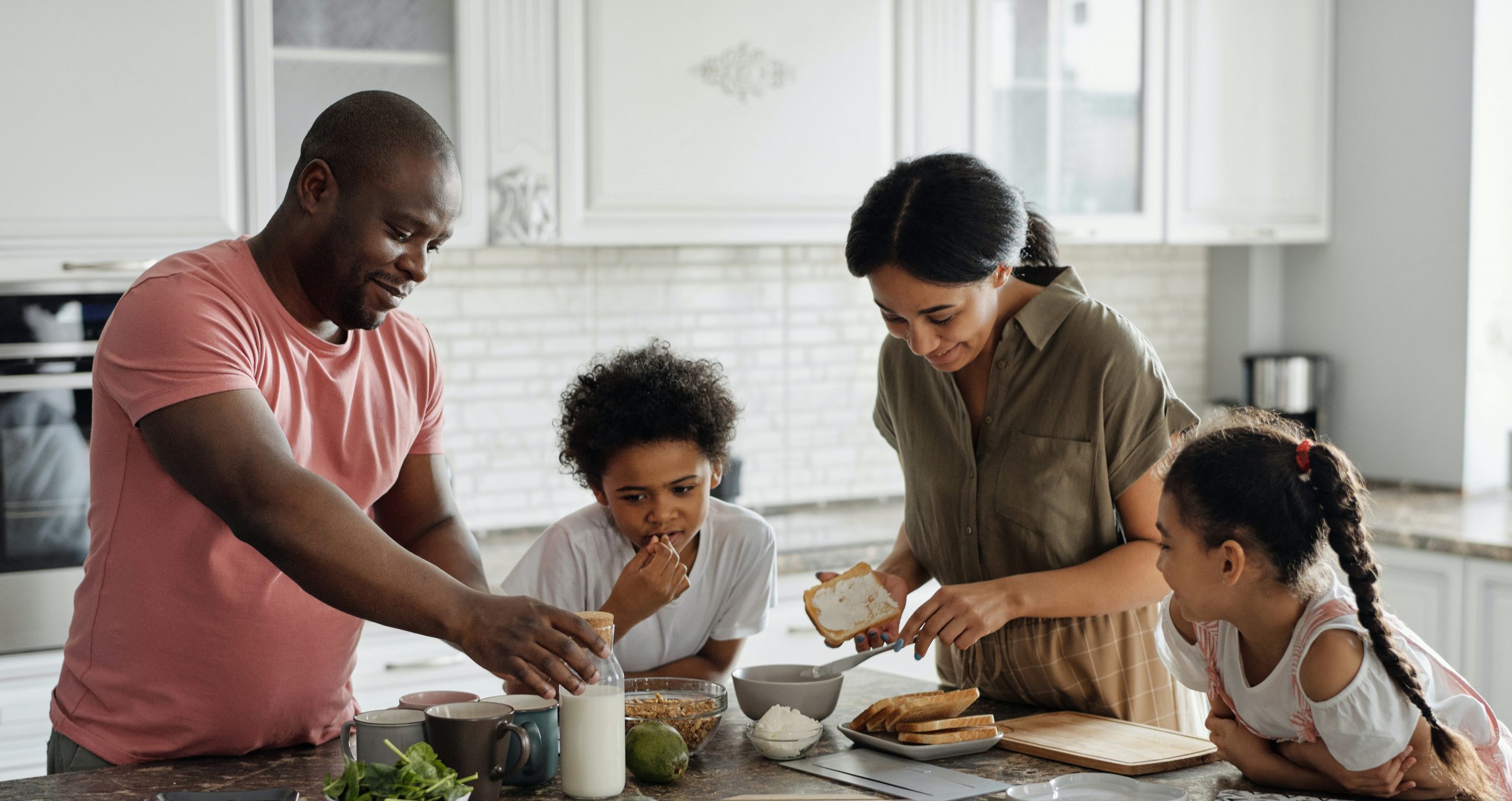 Father, mother, and two children lean over kitchen island and make a sandwich together