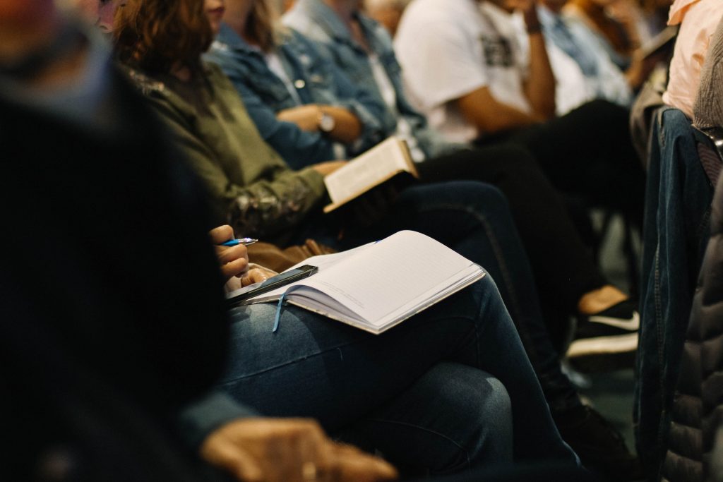 Group of adults sitting. Some adults have notebooks on their laps. 