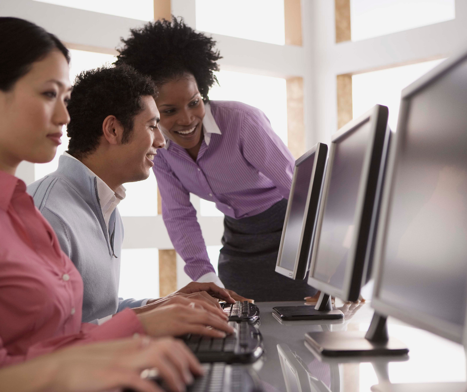 Adults sitting at computers typing. Two adults in a conversation while looking at the computer screen.