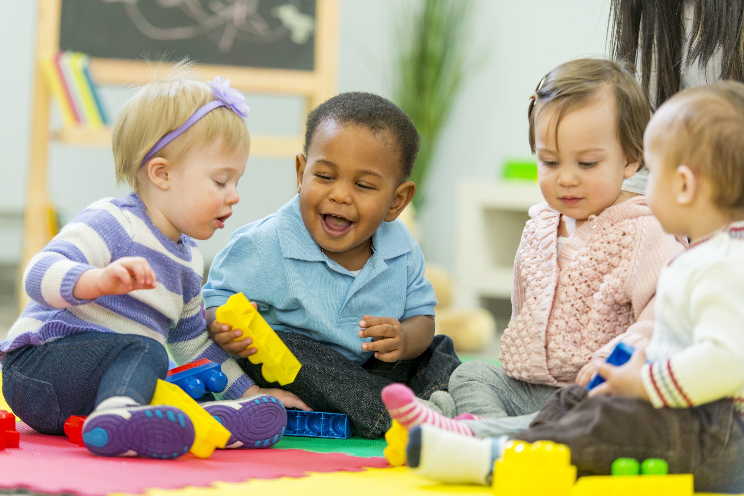 Four infants sitting in a group with some holding interlocking bricks 