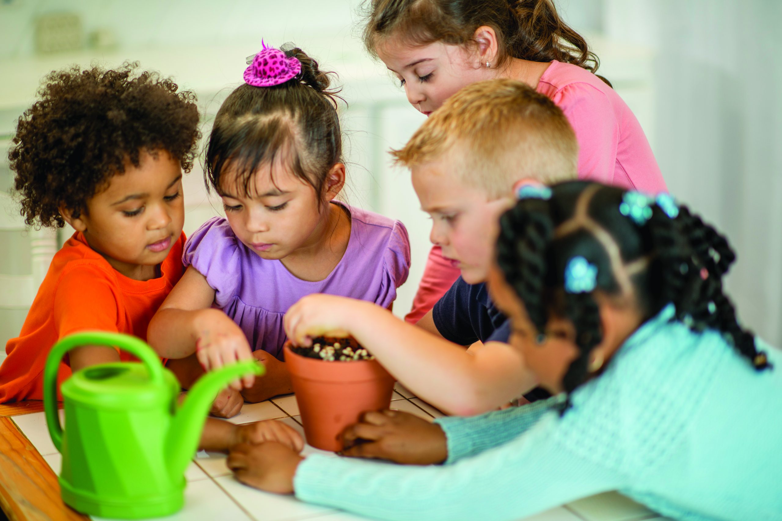 Children planting seeds into a pot full of soil.