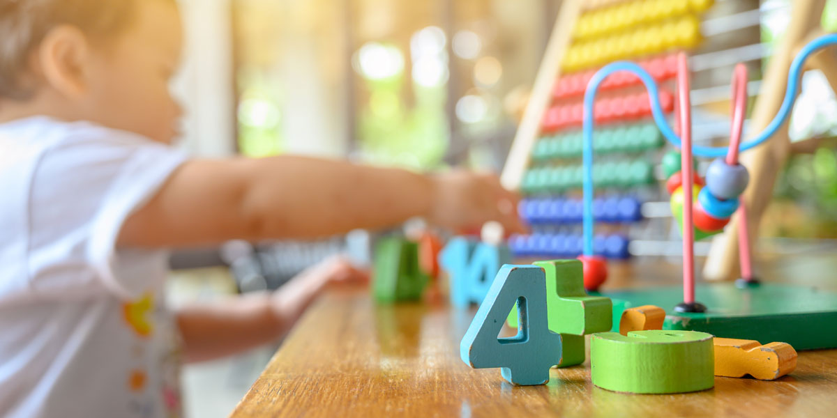 image of a preschool child playing with an abacus in the background. Number blocks are in the foreground with the number 4 highlighted.