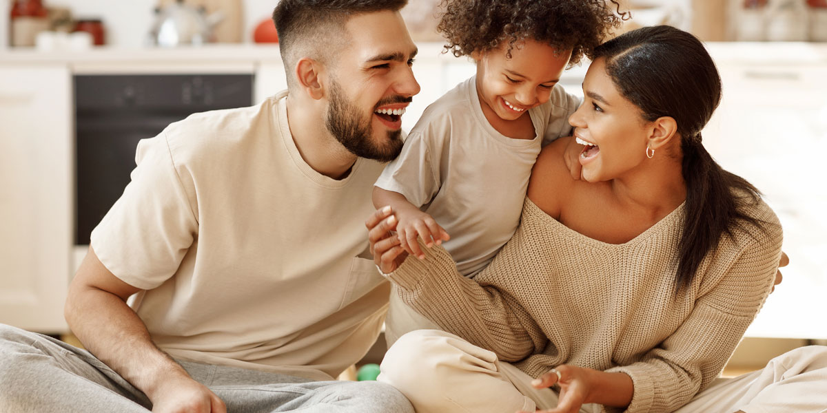 image of a mixed race family, two parents and a young boy, sitting on the floor and smiling at each other.