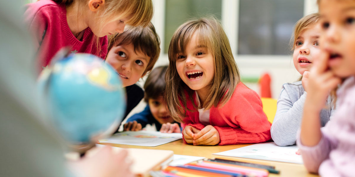 A group of children some are looking at an adult, one is laughing, and one is looking at a paper on the table.